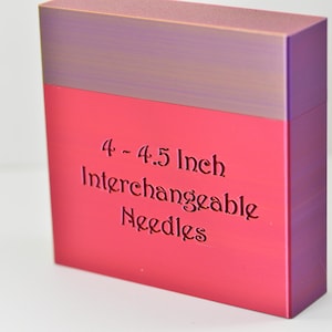 Peut inclure: Une boîte rectangulaire avec un dégradé de couleurs, passant d'un dessus violet à une section inférieure rose vif. La boîte porte l'inscription "4 - 4.5 Inch Interchangeable Needles" en caractères foncés.