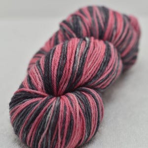 May include: A close-up of three skeins of yarn. The yarn is a blend of pink, gray, and white. The yarn is tightly wound and has a soft, textured appearance. The skeins are arranged in a row, with the closest one in focus.
