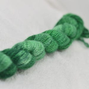 May include: A skein of green yarn, tightly wound and arranged in a row. The yarn has varying shades of green, creating a textured appearance. The yarn is likely used for knitting or crocheting projects.