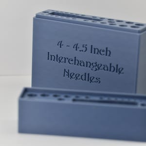 May include: Two blue needle holders, one rectangular and one square, are displayed against a white background. The larger holder has the text "4 - 4.5 Inch Interchangeable Needles" engraved on its front. Both holders have multiple holes.