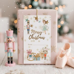 May include: A pink gift box with a "Merry Christmas" gift tag featuring illustrations of a nutcracker, ballerina, and other holiday elements. A pink nutcracker and ballet shoes are on the left and right sides of the gift box.