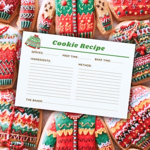 May include: An overhead shot of several sweater-shaped cookies with intricate icing designs in red, green, and white. A recipe card with the title "Cookie Recipe" is in the center. The cookies are arranged on a light-colored surface.