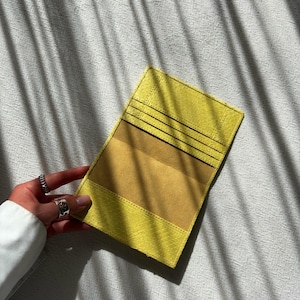 May include: A yellow leather wallet with a textured finish. The wallet has multiple card slots and a contrasting tan interior. The wallet is open, revealing the interior design. The wallet is rectangular in shape.