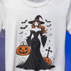 Może przedstawiać: Biała koszulka z ilustracją o tematyce Halloween. Grafika przedstawia wiedźmę w czarnej sukni i kapeluszu, trzymającą dynię. Nietoperze i gwiazdy otaczają wiedźmę, z krzyżem i dynią w tle.