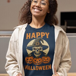 May include: Navy blue t-shirt with a Halloween design. The graphic features a skull wearing a witch hat, three carved pumpkins, and the words "HAPPY HALLOWEEN" in orange. The person is wearing a light beige jacket.