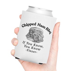 May include: A white foam can cooler featuring a black graphic of a chipped ham sandwich. The text reads Chipped Ham Bbq, If You Know, You Know, and -Yinzer- in a black serif font. The cooler is designed to fit a standard beverage can.