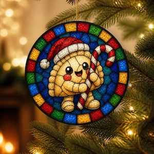 May include: A circular stained glass ornament featuring a smiling, anthropomorphic dumpling wearing a red and white Santa hat and holding a red and white striped candy cane. The design is framed by a border of small, multicolored glass squares.