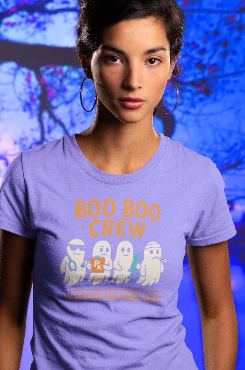 May include: A lilac-colored t-shirt with the text "BOO BOO CREW" in orange. Below the text are four cartoon ghosts dressed as medical professionals. The phrase "HAUNTING THE NIGHT SHIFT" is printed below the ghosts.