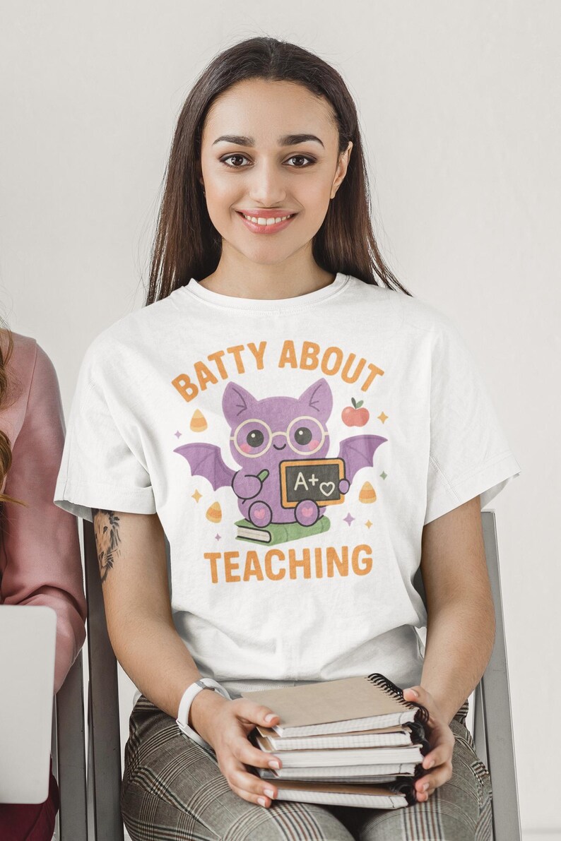 May include: White t-shirt featuring a purple bat wearing glasses and holding a chalkboard with "A+♡". The text "BATTY ABOUT TEACHING" is arched above the bat. The shirt is worn by a person.