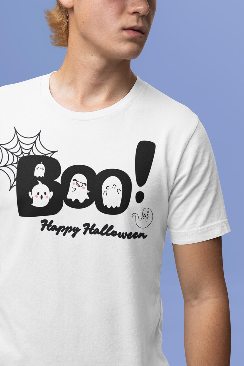 May include: White t-shirt with a Halloween-themed graphic. The design features the word "Boo!" in a black, bold font, with cute ghost illustrations and the text "Happy Halloween" below. A spiderweb is on the left.