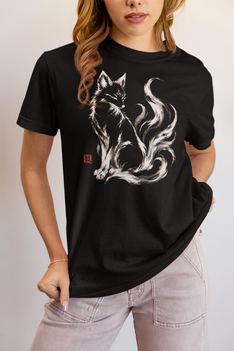 May include: A black short-sleeved t-shirt featuring a white brushstroke-style illustration of a multi-tailed fox sitting in profile. To the left of the fox is a small red square stamp containing the Japanese kanji character for fox.