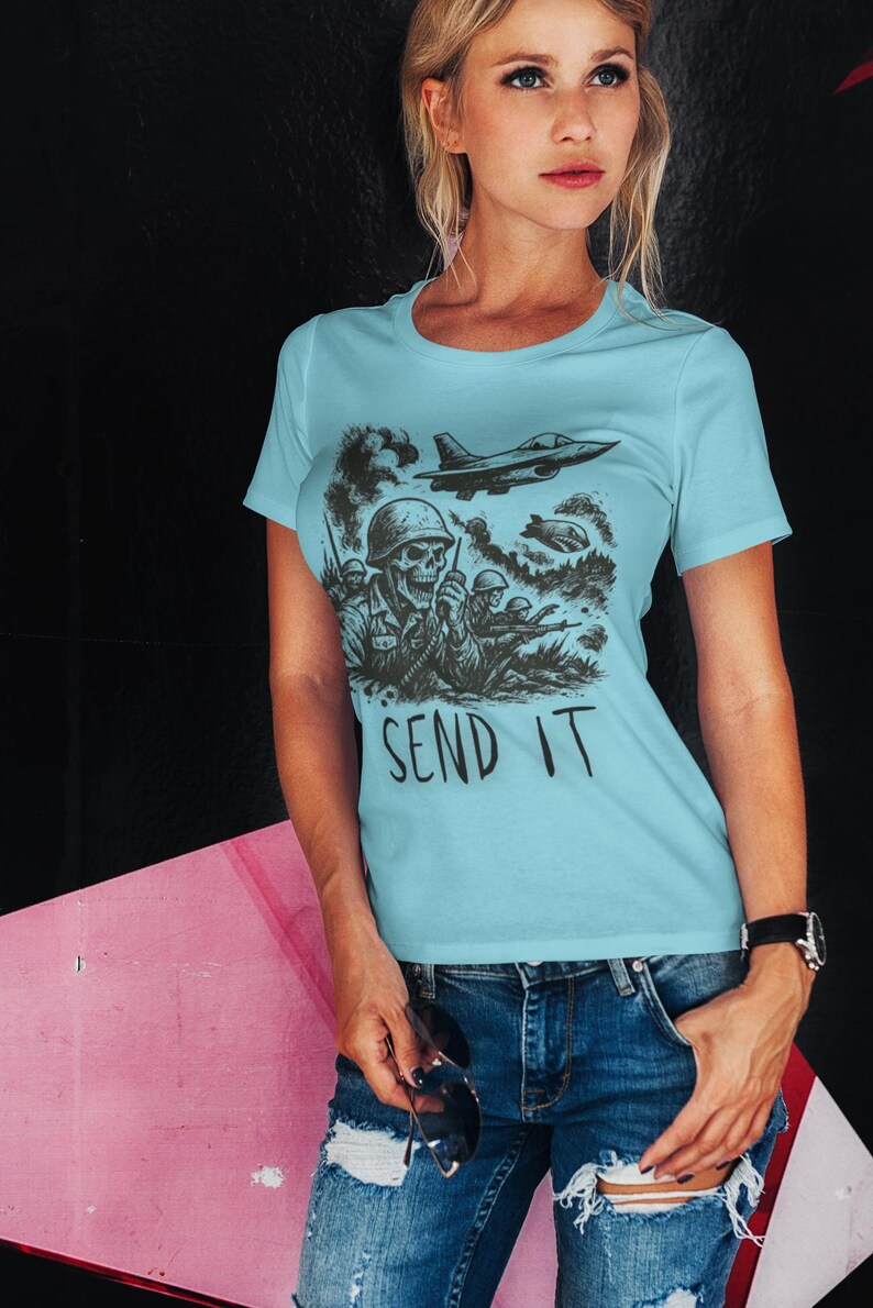 Puede incluir: Camiseta azul claro con un gr&aacute;fico negro de un soldado calavera, aviones militares y el texto "SEND IT". La camiseta es de cuello redondo.