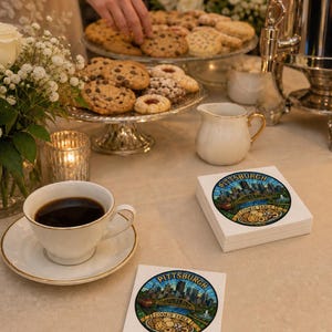 Pu&ograve; includere: Una pila di tovaglioli di carta quadrati e un singolo tovagliolo con un'illustrazione circolare dello skyline di Pittsburgh, un ponte giallo e vari biscotti con il testo Pittsburgh Cookie Table stampato in uno stile a vetrata.