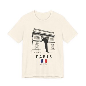 Puede incluir: Camiseta color crema con una ilustraci&oacute;n en blanco y negro del Arco del Triunfo de Par&iacute;s. Debajo de la imagen, la palabra "PARIS" est&aacute; impresa, junto con la bandera francesa y la palabra "FRANCE".