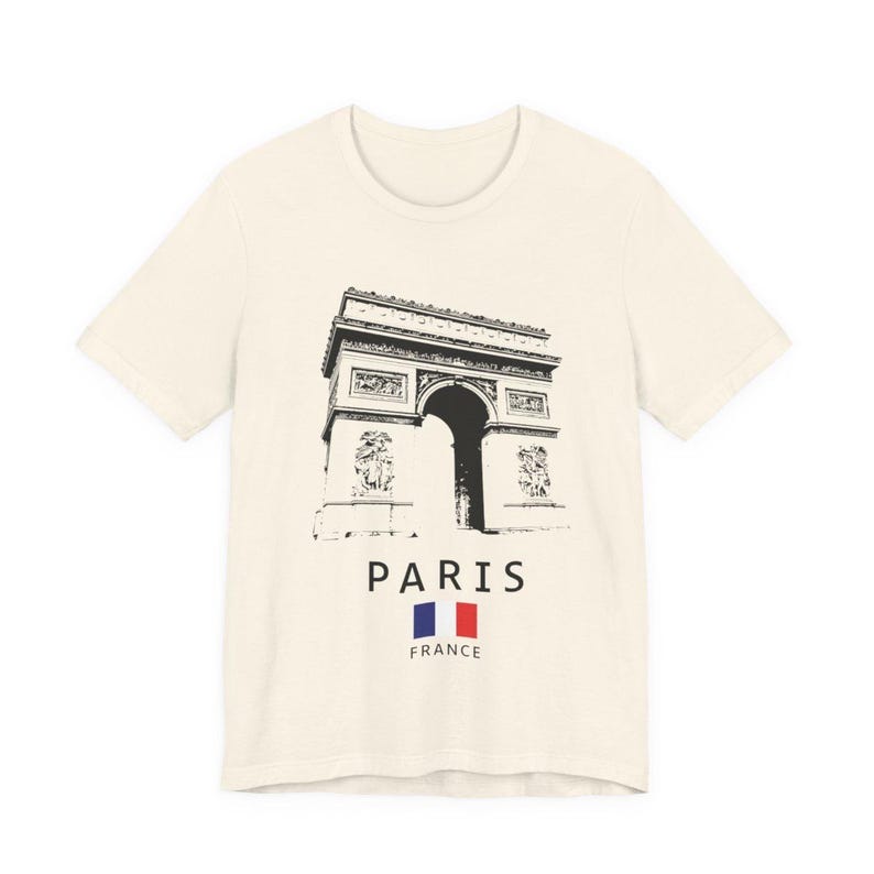 Puede incluir: Camiseta color crema con una ilustraci&oacute;n en blanco y negro del Arco del Triunfo de Par&iacute;s. Debajo de la imagen, la palabra "PARIS" est&aacute; impresa, junto con la bandera francesa y la palabra "FRANCE".