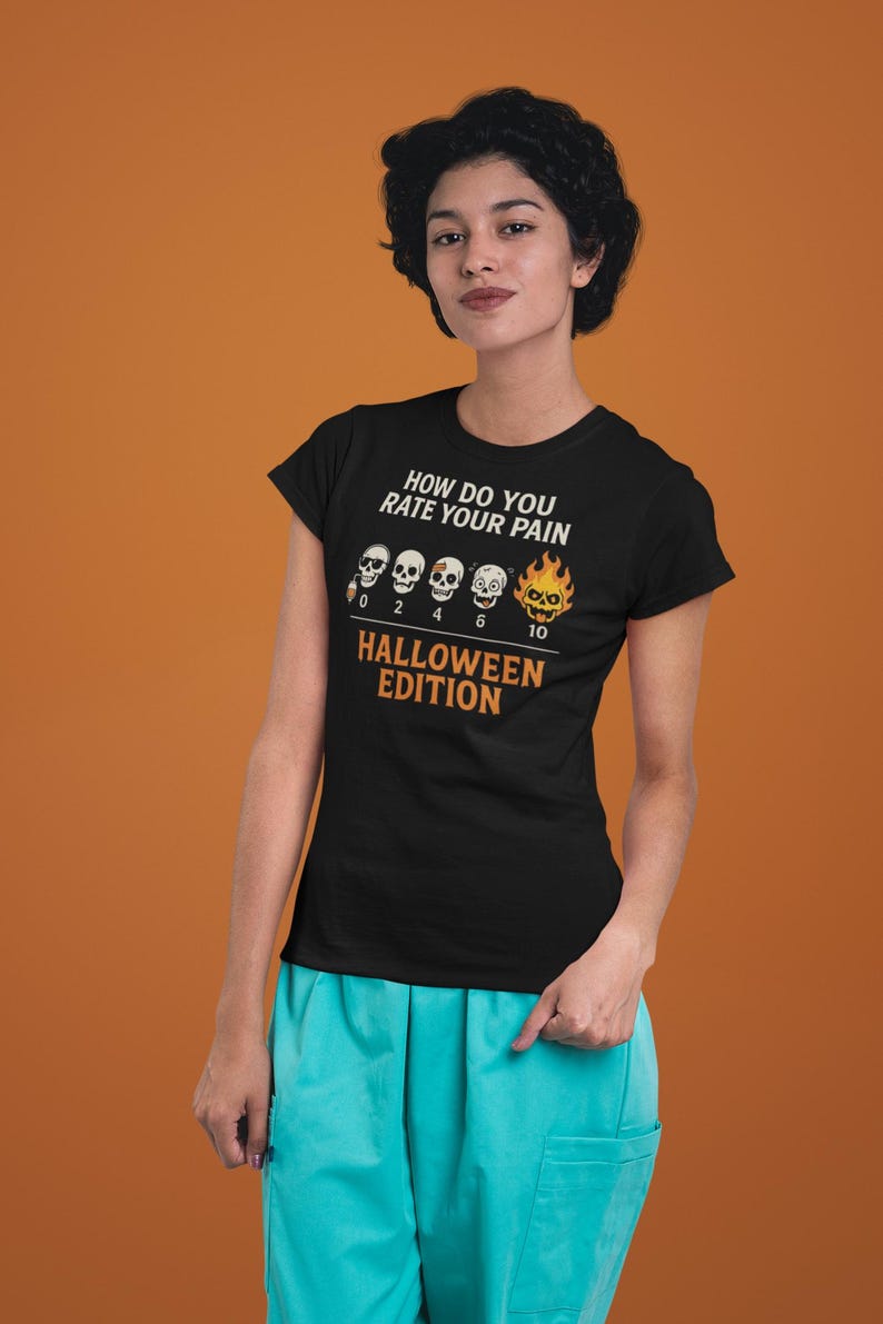 May include: Black t-shirt with the text "HOW DO YOU RATE YOUR PAIN" and "HALLOWEEN EDITION". The shirt features a pain scale with skull graphics. The person is wearing turquoise scrubs.