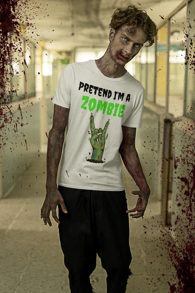 May include: White t-shirt with the text "PRETEND I'M A ZOMBIE" in black and green. The shirt features a green hand making a rock and roll gesture. The person is wearing black pinstripe pants. The background is a hallway with blood splatter.