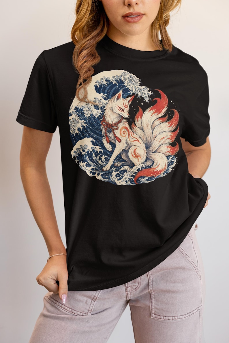 May include: A black short-sleeve t-shirt featuring a circular graphic print of a white multi-tailed fox with red markings and a red rope collar, positioned in front of a stylized blue and white ocean wave design inspired by traditional Japanese art.