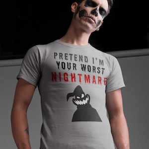 May include: A grey t-shirt with the slogan "PRETEND I'M YOUR WORST NIGHTMARE" in black and red. A black silhouette of a spooky character is below the text. The t-shirt has short sleeves.