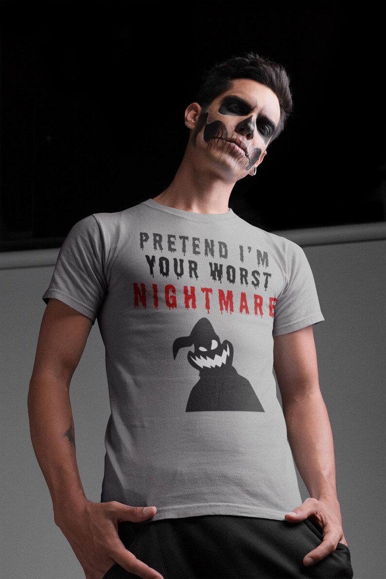 May include: A grey t-shirt with the slogan "PRETEND I'M YOUR WORST NIGHTMARE" in black and red. A black silhouette of a spooky character is below the text. The t-shirt has short sleeves.