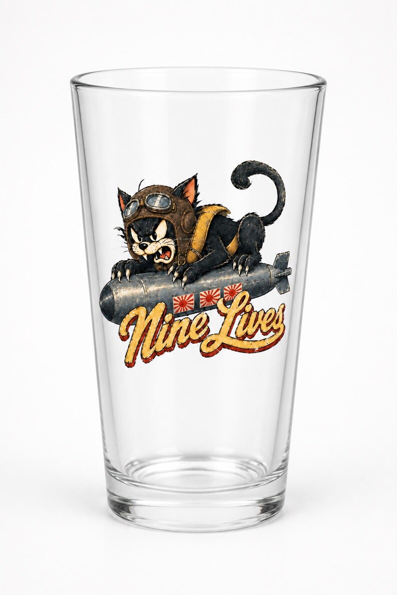 Op de afbeelding: Een helder glazen drinkglas met een afbeelding van een zwarte kat met een bruine vliegeniersmuts en een bril, rijdend op een grijze bom. Onder de bom staat de tekst Nine Lives in een geel en rood lettertype met drie kleine zonnesymbolen.