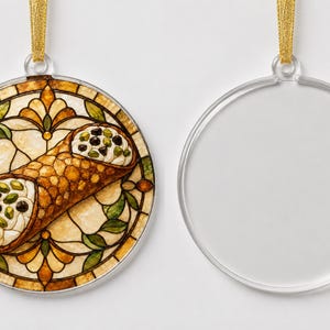 May include: A round, flat, clear acrylic ornament featuring a printed illustration of a cannoli filled with cream, chocolate chips, and pistachios, set against a stained-glass style background with gold ribbon for hanging. A second blank ornament is shown.