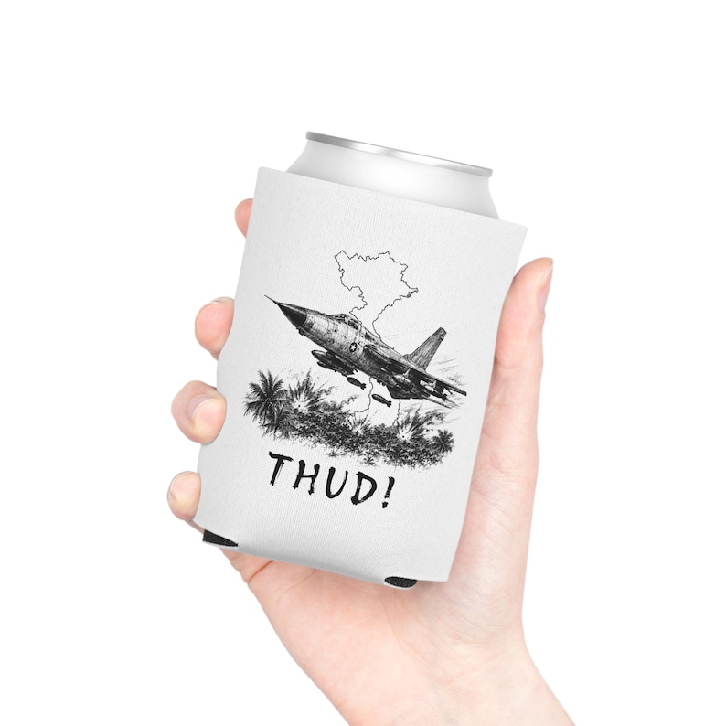 May include: A white foam can cooler featuring a black and white ink-style illustration of a fighter jet flying over a map outline and jungle foliage, with the word THUD! printed in bold, distressed capital letters below the graphic design.