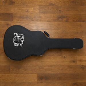 Może przedstawiać: Czarny futerał na gitarę z białą naklejką przedstawiającą grafikę czaszki w hełmie wojskowym, samolot myśliwski oraz napis SEND IT wydrukowany pogrubioną wielką czcionką w dolnej części naklejki.