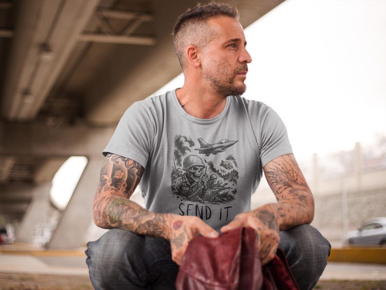 Puede incluir: Camiseta gris claro con un gr&aacute;fico de tem&aacute;tica militar. El dise&ntilde;o presenta un soldado calavera, un avi&oacute;n a reacci&oacute;n y el texto "SEND IT" en blanco y negro. La camiseta est&aacute; hecha de un material suave.
