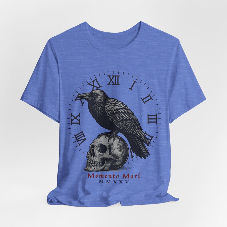 May include: Blue t-shirt featuring a black raven perched atop a skull. A clock face with Roman numerals surrounds the raven and skull. The words "Memento Mori" and the Roman numeral "MMXXV" are printed below the skull.