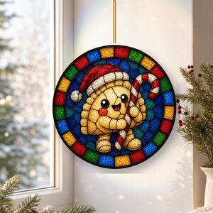 May include: A circular stained glass suncatcher featuring a smiling dumpling character wearing a red and white Santa hat and holding a red and white striped candy cane. The border consists of alternating red, blue, yellow, and green glass tiles.