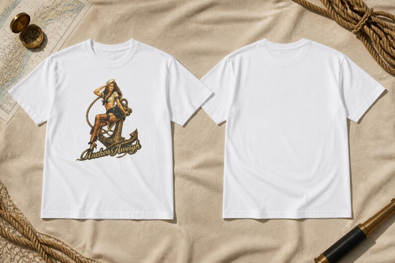 May include: A white short-sleeved t-shirt featuring a graphic print of a pin-up style sailor sitting on a large metal anchor. The text "Anchors Aweigh" is printed in a stylized font below the anchor. The back of the t-shirt is plain white.