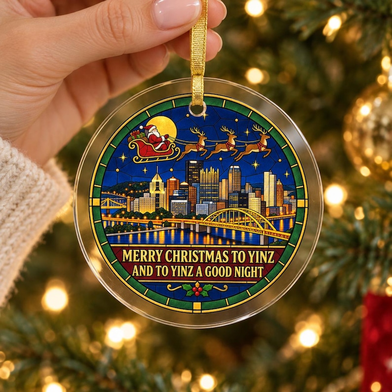 May include: A round, clear acrylic Christmas ornament featuring a stained-glass style illustration of the Pittsburgh skyline at night, with Santa and his reindeer flying above. The text reads, Merry Christmas to Yinz and to Yinz a good night.
