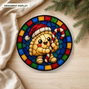 May include: A circular ornament display featuring a stained-glass style illustration of a smiling, golden-brown dumpling character wearing a red and white Santa hat and holding a red and white striped candy cane against a blue background.