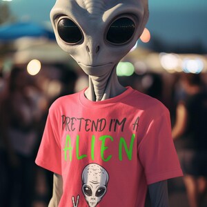 May include: A gray alien with large black eyes wearing a pink t-shirt. The shirt has the text "PRETEND I'M A ALIEN" in green and white, along with a cartoon alien giving a peace sign.
