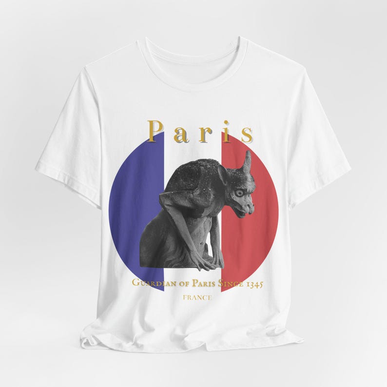 May include: White t-shirt featuring a black and white gargoyle statue in front of a blue and red circle, representing the French flag. The word 'Paris' is in gold letters above the statue. Below the circle, it reads 'Guardian of Paris Since 1345' and 'France'.