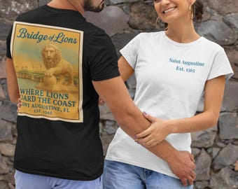 May include: A black t-shirt with a vintage-style graphic on the back that reads "Bridge of Lions" and "Where Lions Guard the Coast, Saint Augustine, FL, Est. 1565." A white t-shirt with "Saint Augustine Est. 1565" in blue text is also visible.