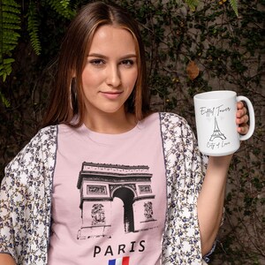 May include: A woman wearing a pink t-shirt with a black graphic of the Arc de Triomphe and the word "PARIS" below it. She is also holding a white mug with the Eiffel Tower and the words "City of Love" printed on it. She is wearing a floral patterned kimono.