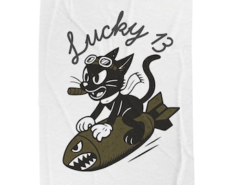 May include: A white blanket featuring a cartoon illustration of a black cat riding a bomb. The cat wears goggles and a scarf, holding a cigar. The words "Lucky 13" are written above the cat in a vintage font.