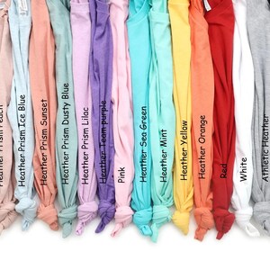 Puede incluir: Una colecci&oacute;n de camisetas de varios colores, incluyendo menta, melocot&oacute;n, azul hielo, puesta de sol, azul polvoriento, lila, equipo p&uacute;rpura, rosa, verde mar, amarillo, naranja, rojo, blanco, brezo atl&eacute;tico y negro. Cada camiseta est&aacute; etiquetada.