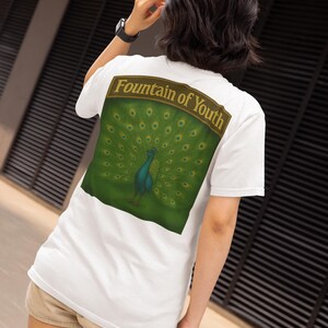 May include: White t-shirt with a large graphic on the back featuring a peacock with its feathers fanned out. The graphic is set against a green background with the words "Fountain of Youth" above the peacock.