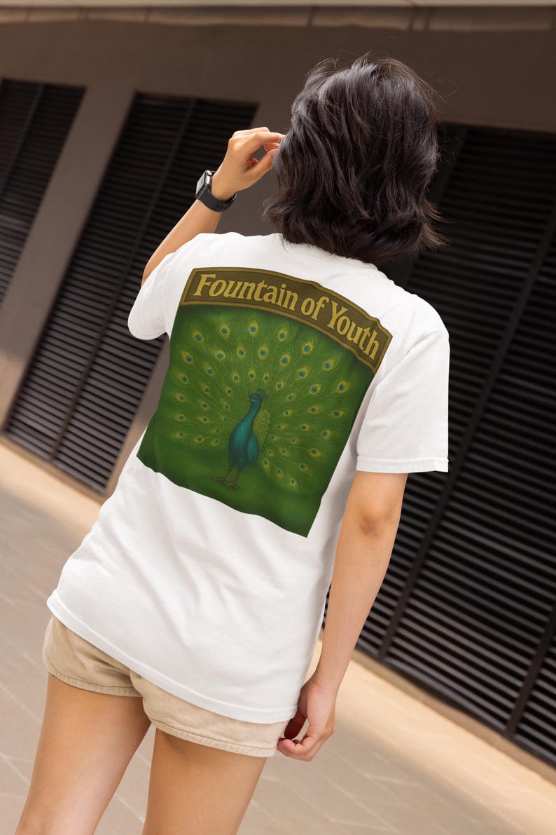 May include: White t-shirt with a large graphic on the back featuring a peacock with its feathers fanned out. The graphic is set against a green background with the words "Fountain of Youth" above the peacock.