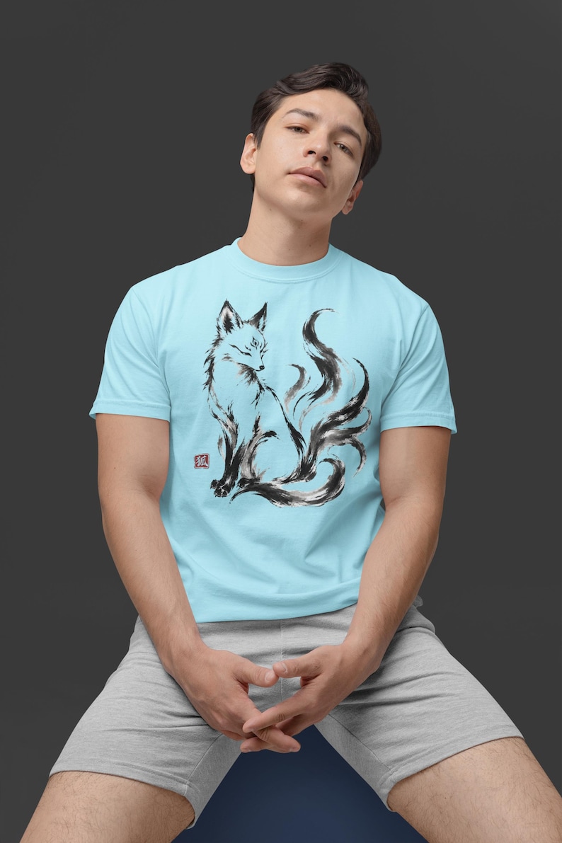 K&ouml;nnte beinhalten: Ein hellblaues T-Shirt mit kurzen &Auml;rmeln und einer schwarz-wei&szlig;en Tuschezeichnung eines mehrschw&auml;nzigen Fuchses im Profil. Die Grafik enth&auml;lt einen kleinen roten quadratischen Stempel mit einem japanischen Schriftzeichen links.