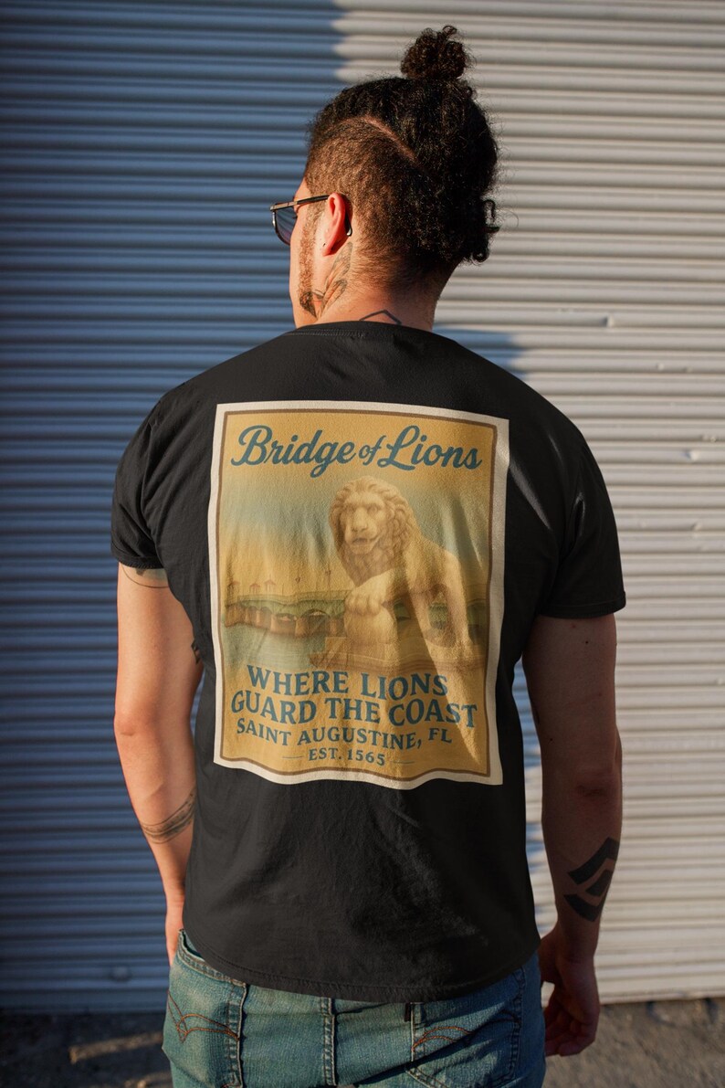 Może przedstawiać: Czarny t-shirt z grafiką w stylu vintage na plecach. Grafika przedstawia posąg lwa na moście z napisem "Bridge of Lions" i "Where Lions Guard the Coast, Saint Augustine, FL, EST. 1565."