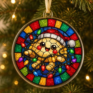 May include: A round Christmas ornament featuring a stained-glass style design of a smiling turtle wearing a Santa hat and tangled in colorful string lights. The border consists of alternating red, blue, yellow, and green glass-like segments.
