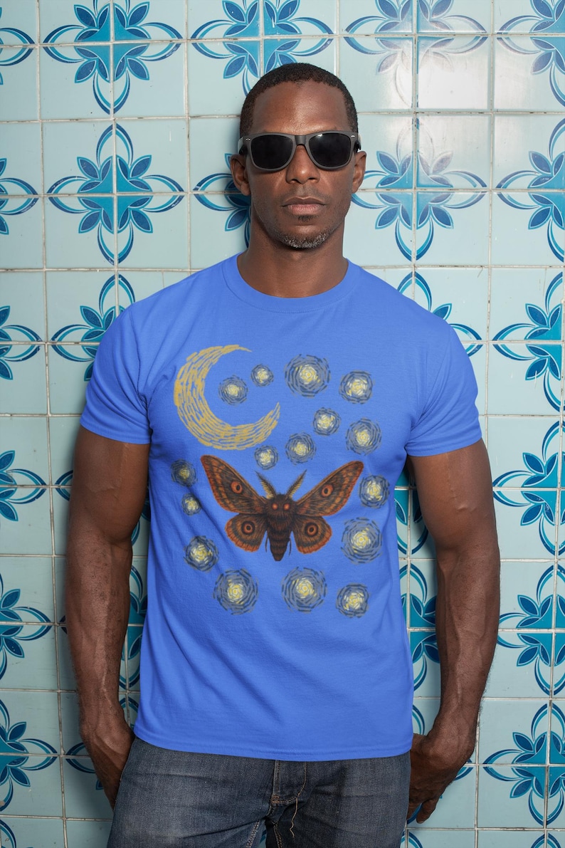 May include: A blue t-shirt featuring a moth design in a Van Gogh style. The moth is brown with orange accents, set against a yellow crescent moon and swirling yellow stars. The shirt is worn by a person wearing sunglasses.