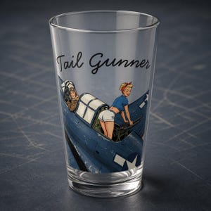 May include: A clear glass pint tumbler featuring a graphic illustration of a blue military aircraft with a pilot in the cockpit and a person in a blue shirt and white shorts operating a machine gun. The text Tail Gunner is printed in black.