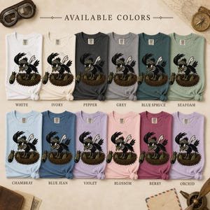 Puede incluir: Una colecci&oacute;n de doce camisetas de varios colores, cada una con un gr&aacute;fico de un p&aacute;jaro con gafas protectoras en un nido con bombas. El texto "AVAILABLE COLORS" est&aacute; impreso en la parte superior, con los nombres de los colores debajo.