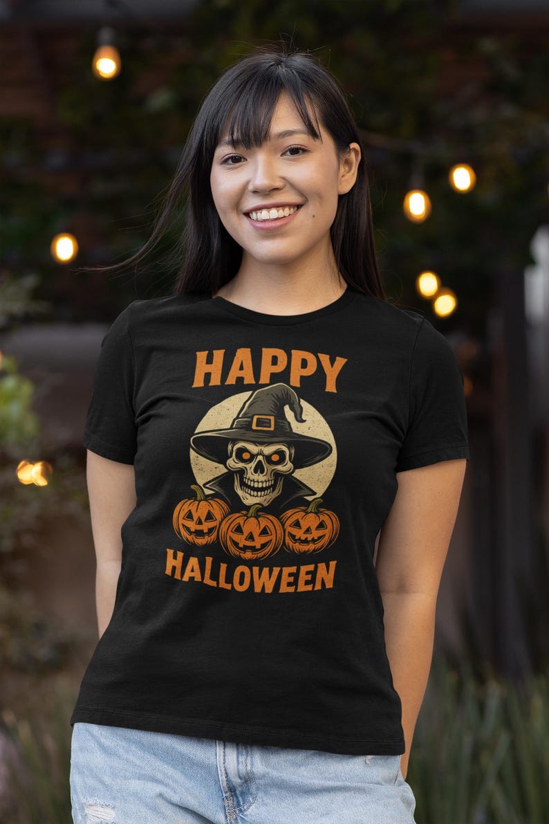 May include: Black t-shirt with an orange and white Halloween graphic. The graphic features a skull wearing a witch hat, with three jack-o'-lanterns below and the words "HAPPY HALLOWEEN" in orange.