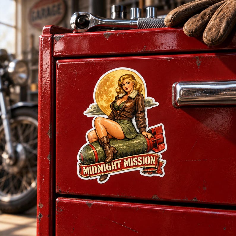 K&ouml;nnte beinhalten: Ein Aufkleber mit einer Pin-up-Illustration einer Person mit blondem Haar, die eine braune Bomberjacke und einen gr&uuml;nen Rock tr&auml;gt und auf einer gr&uuml;nen Bombe vor einem gelben Mond sitzt, mit einem roten Banner mit der Aufschrift MIDNIGHT MISSION.